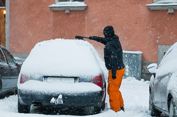 Man sopar bort snö från bil.